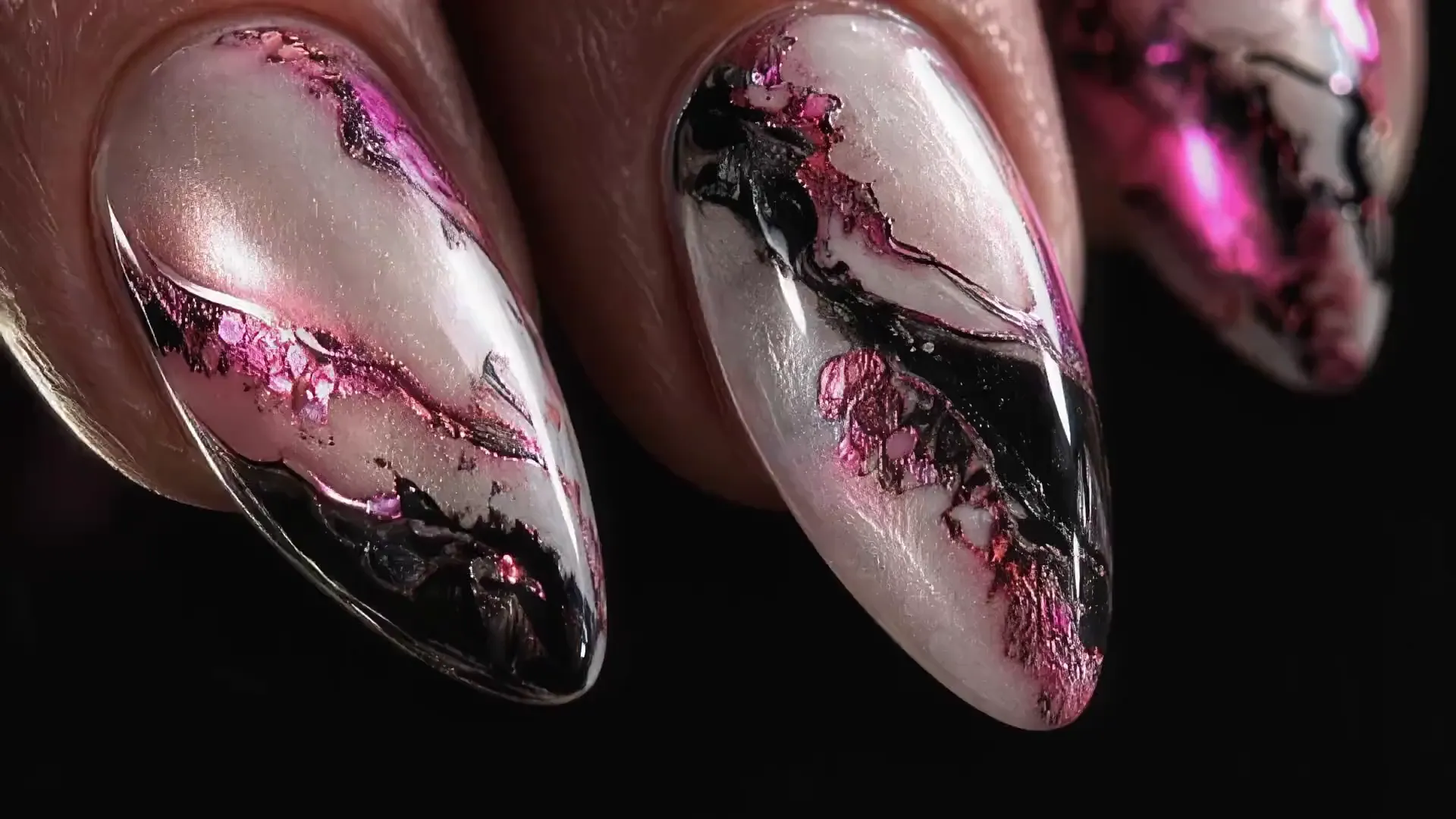 A macro of three almond nails, pearl with pink chrome and black foil, lit from one side.